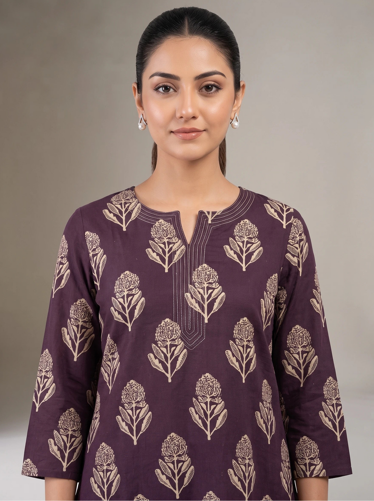 A woman wearing a dark purple kurta with beige floral block prints, photographed against a neutral gray studio background.