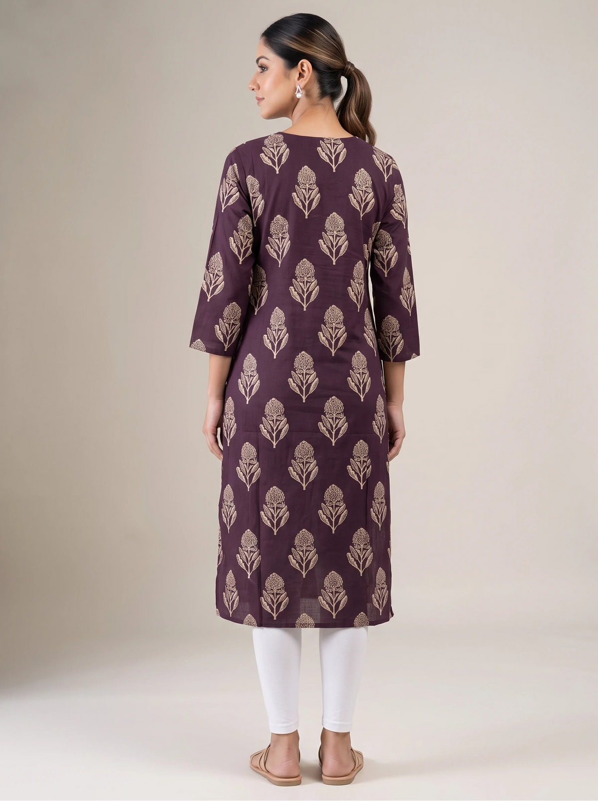 A woman shown from the back wearing a knee-length purple kurta with a beige floral block print, paired with white leggings and beige flat sandals, against a neutral beige studio background.