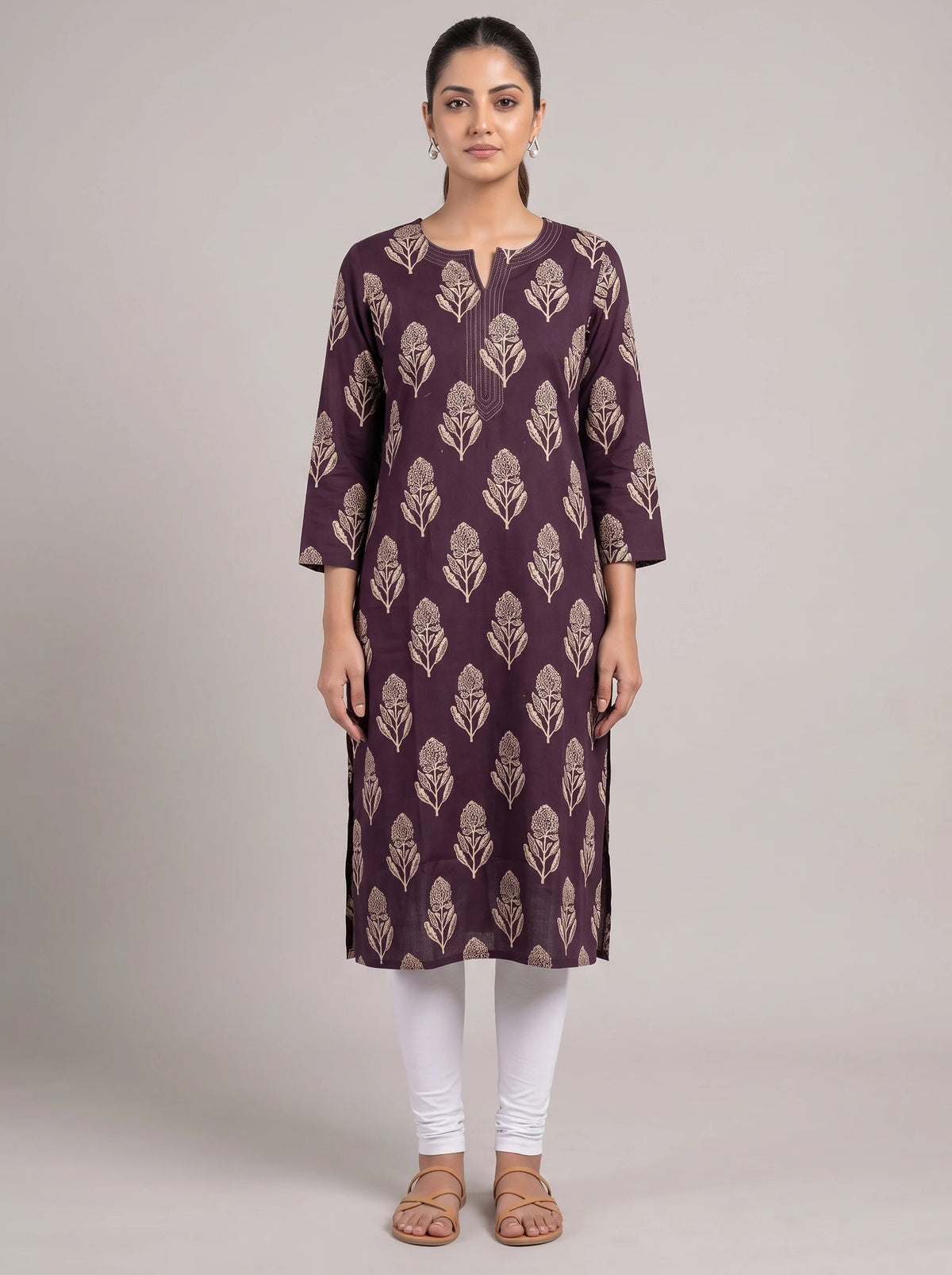 A woman modeling a three-quarter sleeve kurta in deep purple with a beige leaf block print pattern, paired with white leggings and brown sandals, against a solid light gray studio background.