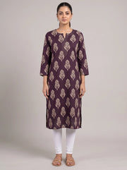 A woman modeling a three-quarter sleeve kurta in deep purple with a beige leaf block print pattern, paired with white leggings and brown sandals, against a solid light gray studio background.