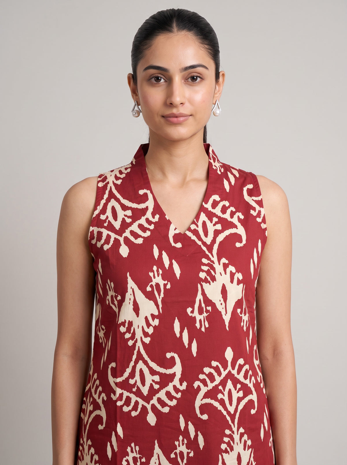 A woman modeling a sleeveless red top with a cream ikat pattern, shot against a solid light gray background.