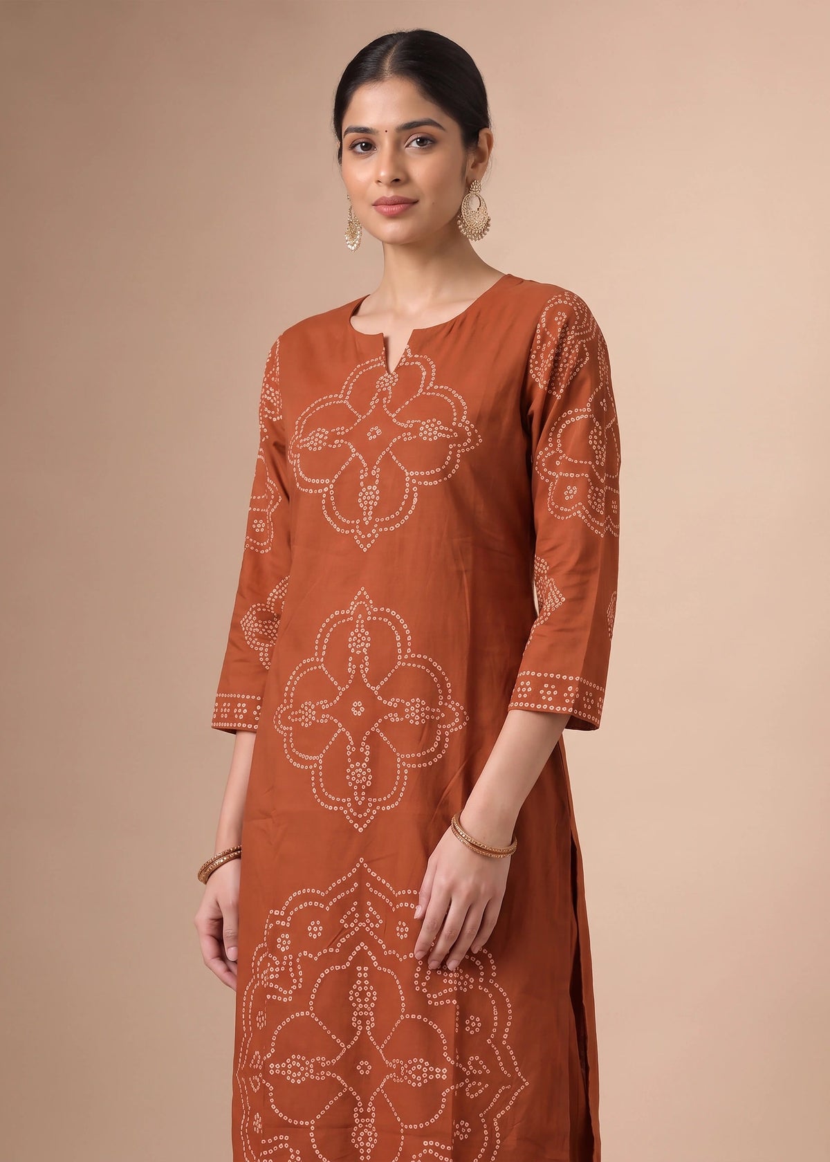 A woman modeling a rust-orange kurta with white block-printed patterns, set against a solid beige studio background.