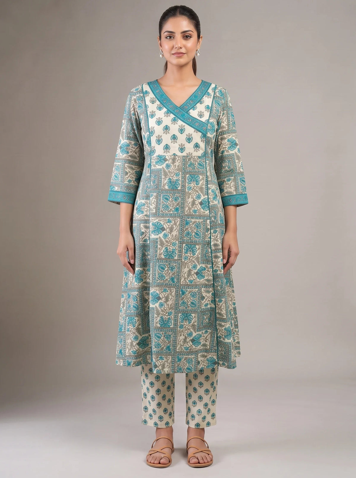 A woman modeling a traditional Indian outfit consisting of a long kurta and matching pants. The outfit features a cream base with teal blue geometric block prints and borders.