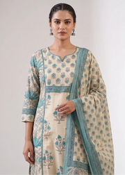 A woman modeling a cream-colored Indian ethnic suit with teal blue floral block prints and a matching dupatta, set against a plain light gray studio background.
